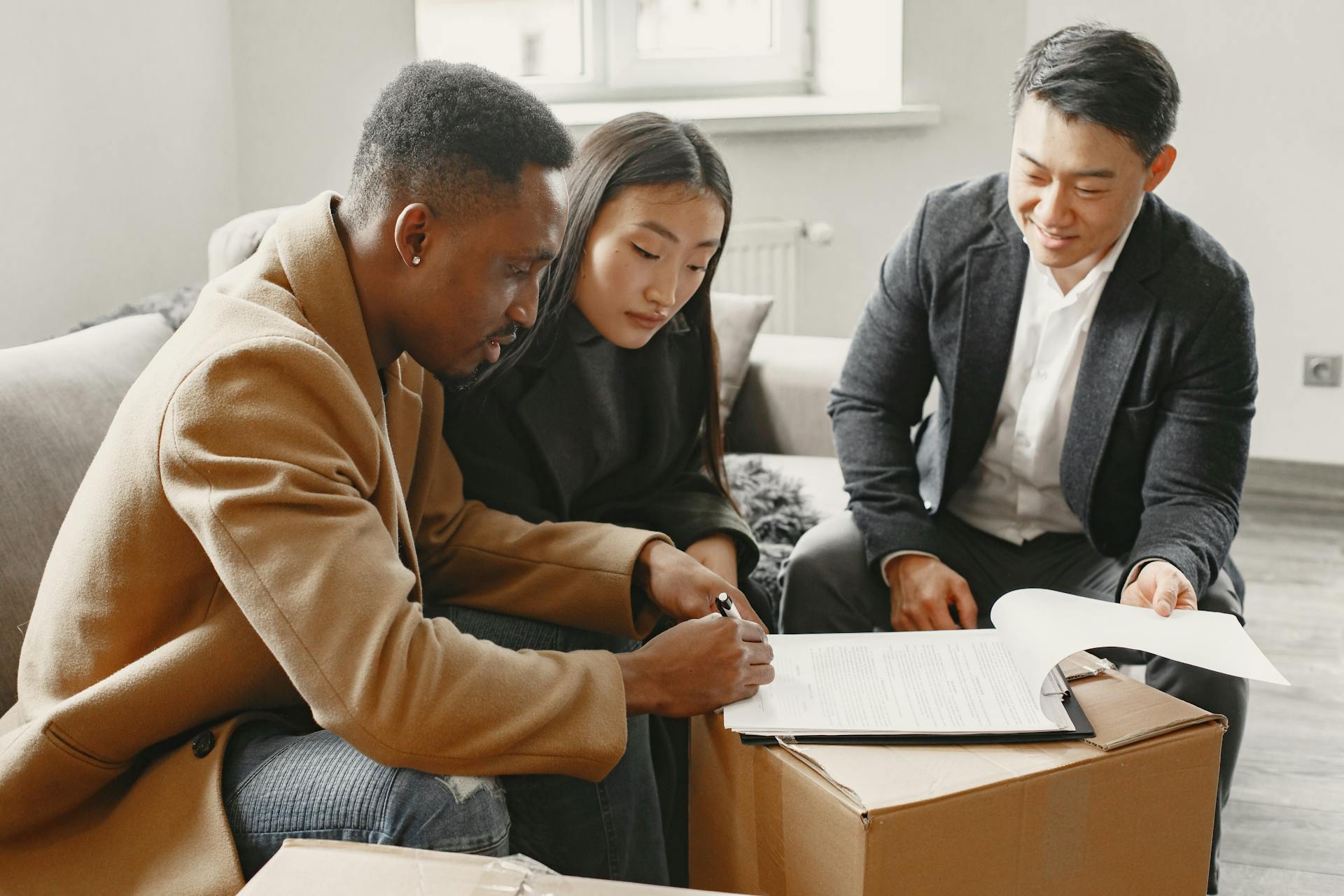 A multiracial couple signing home documents with a realtor indoors.