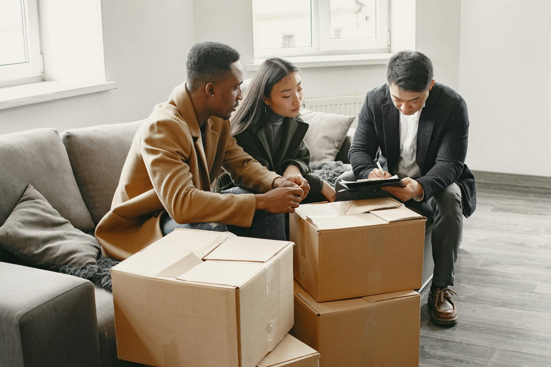 Multiracial couple signing real estate papers at home with a realtor. Cardboard boxes suggest moving in.