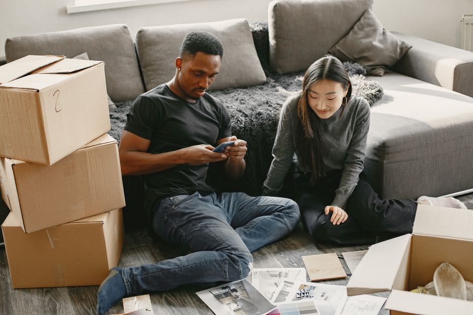Group of young Black Nigerian friends in a bright Manchester living room sorting shared bags of African groceries into separate piles, laughing and chatting, warm evening light, photorealistic