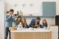 A cheerful family gathers in a modern kitchen enjoying a festive celebration with gifts.