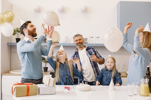 Free A happy family celebrating together indoors with balloons, cake, and gifts. Stock Photo