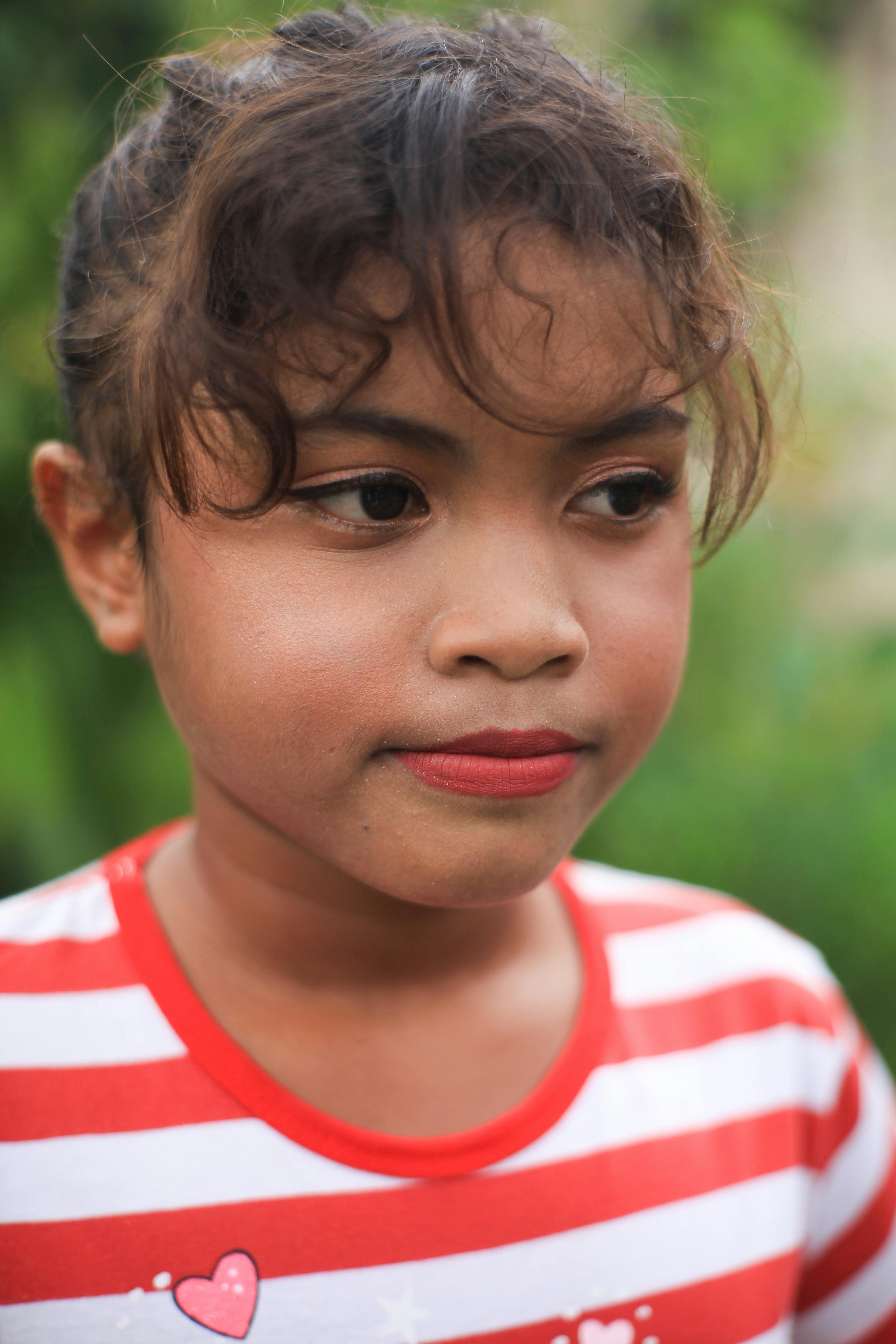Close-up portrait of a young girl with curly hair wearing a red striped shirt outdoors.