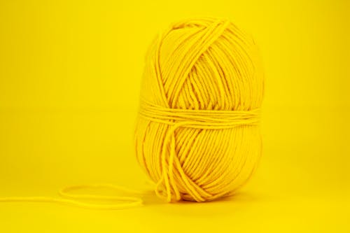 Isolated bright yellow woolen yarn for knitting handicraft placed against vivid yellow background