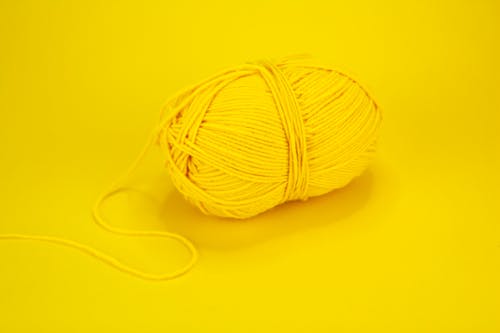 From above of yellow yarn formed in skein with loose thread on yellow background