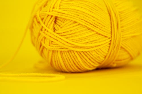 Part of woolen skein for knitting of yellow color with string on vivid surface