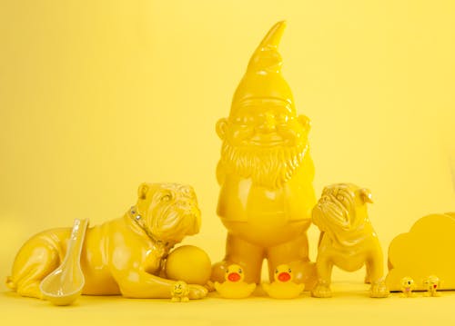 Free Composition of various zoomorphic souvenirs and garden gnome of yellow color placed on yellow surface and background Stock Photo