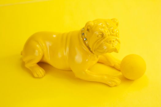 High angle of ceramic souvenir of French bulldog sitting near ball on yellow background