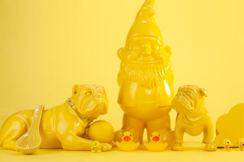 Free Statuettes of yellow bulldogs and ducks and garden gnome with ladle on yellow surface and background Stock Photo