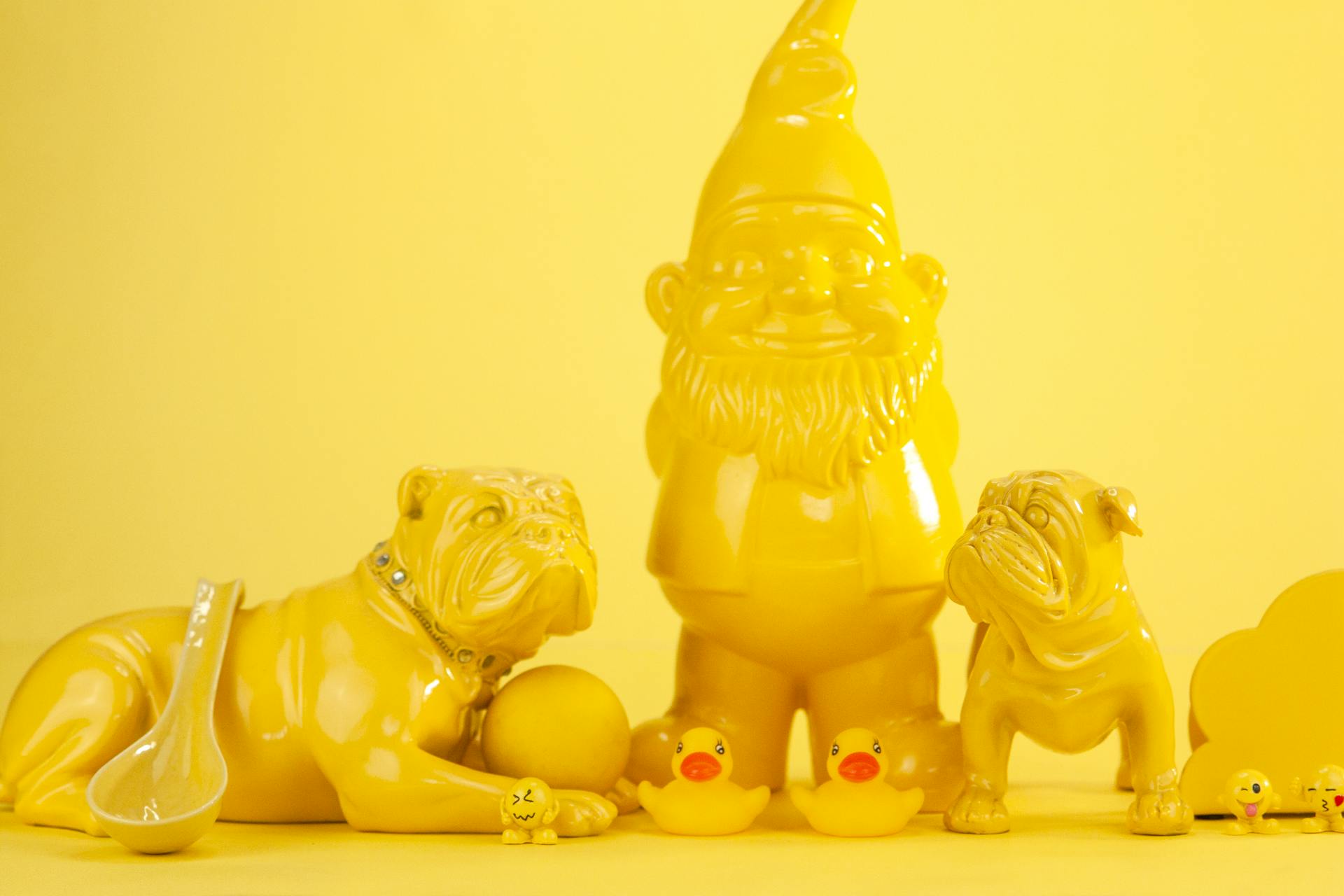 Statuettes of yellow bulldogs and ducks and garden gnome with ladle on yellow surface and background