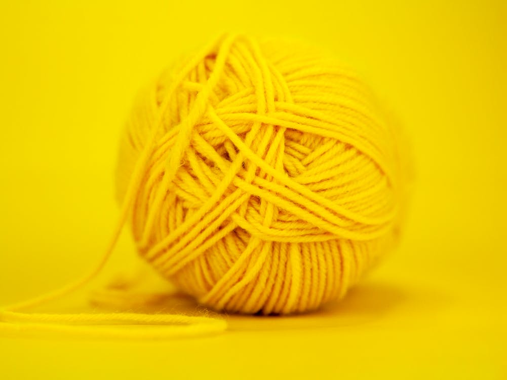 Regular ball of colorful yellow yarn placed on bright monochrome background in soft focus