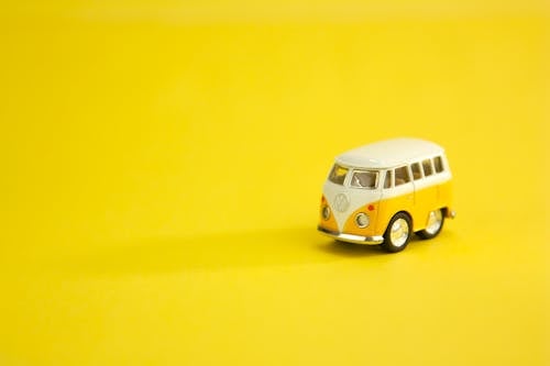 Yellow and white miniature of vintage camping trailer placed on right side of bright yellow surface