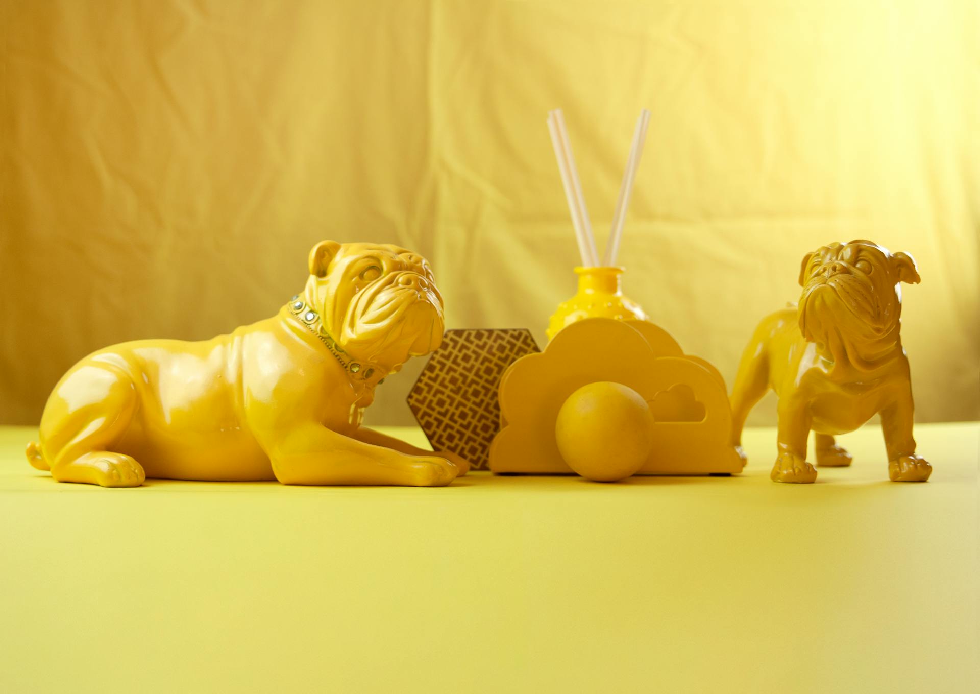 Kleine heldergele speelgoedbulldogs met kraag op een gele tafel met verschillende decoraties op een lichtgele achtergrond