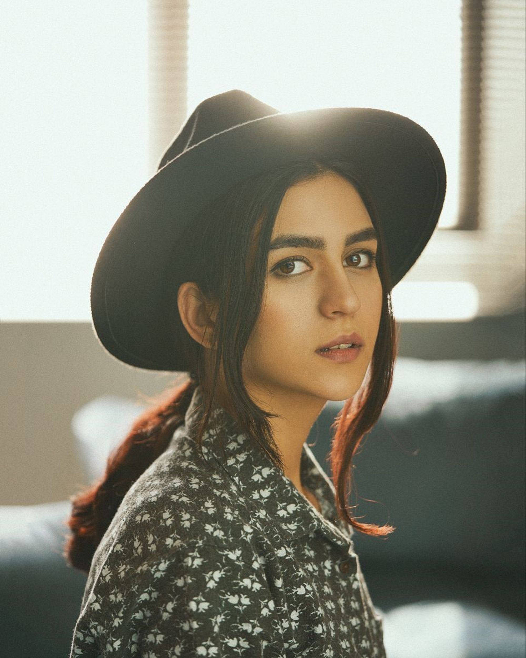Beautiful woman in a black hat, gazing at the camera with soft lighting indoors.