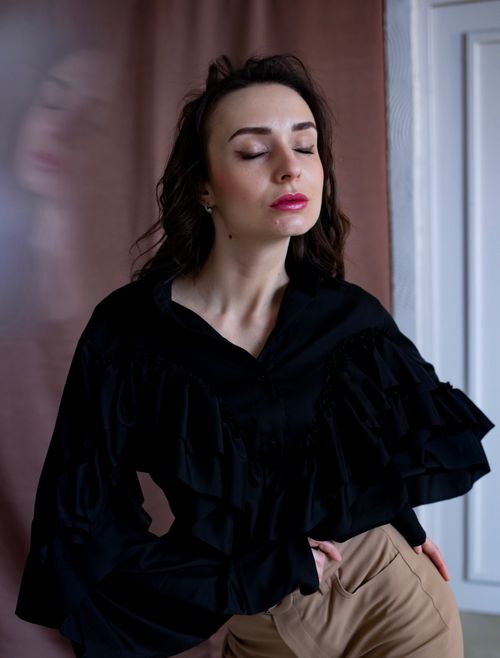Free Elegant woman in a black top with ruffles, eyes closed, enjoying a serene moment indoors. Stock Photo