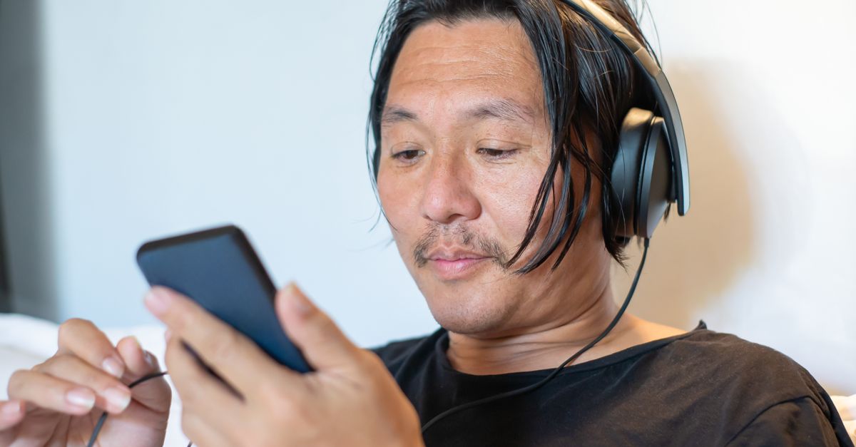 Person wearing headphones crying while looking at phone screen, warm lighting