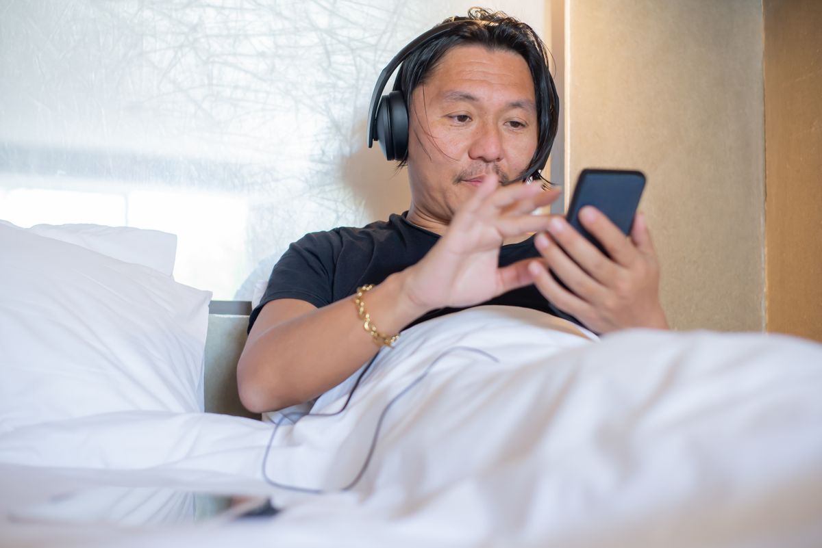A person relaxing on a couch listening to an audiobook through headphones on a smartphone