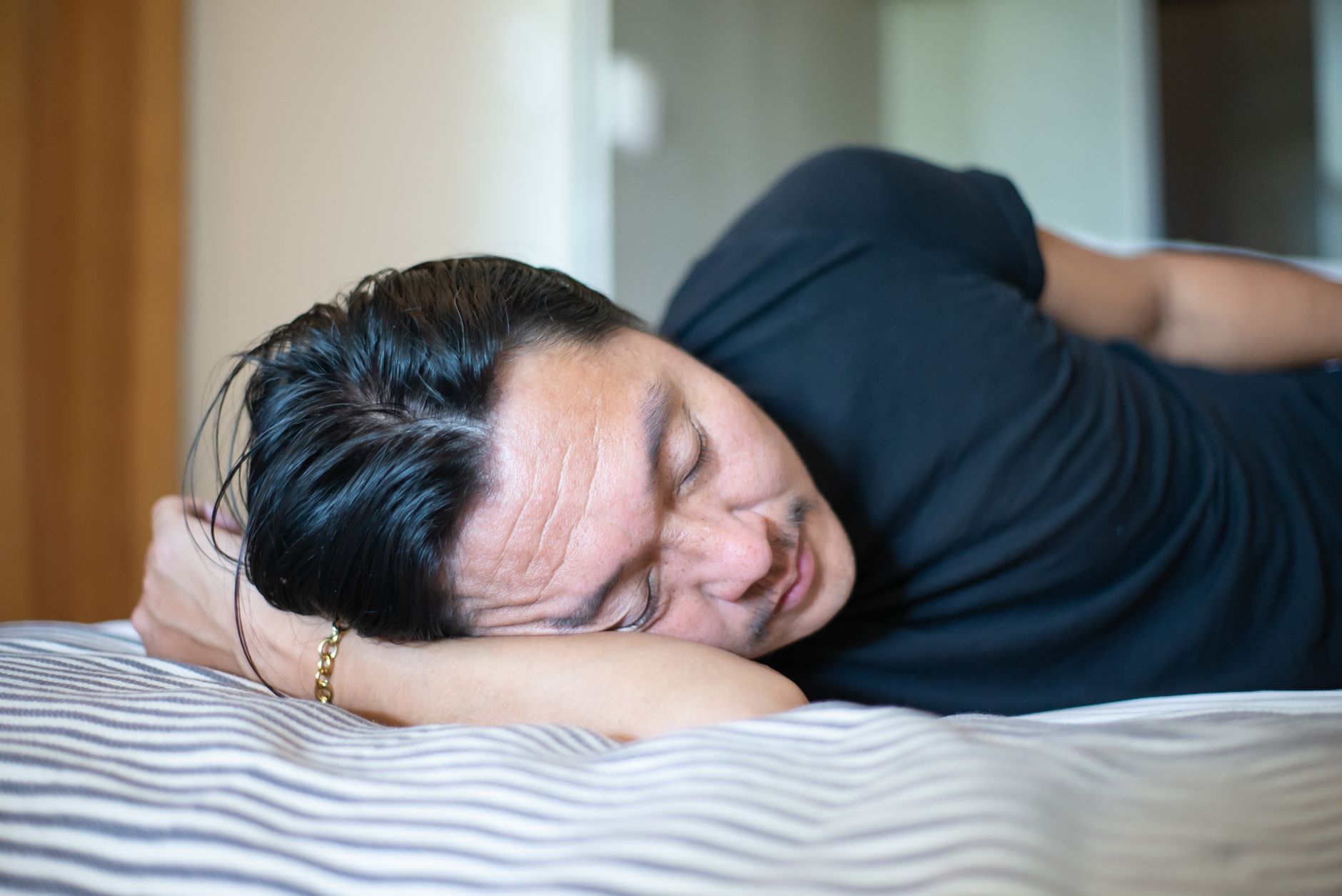 Asian man with facial hair wearing a black shirt asleep indoors, capturing relaxation essence.