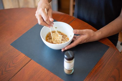Free High-angle view of hands holding a bowl of Asian noodles with chopsticks on a wooden table. Stock Photo