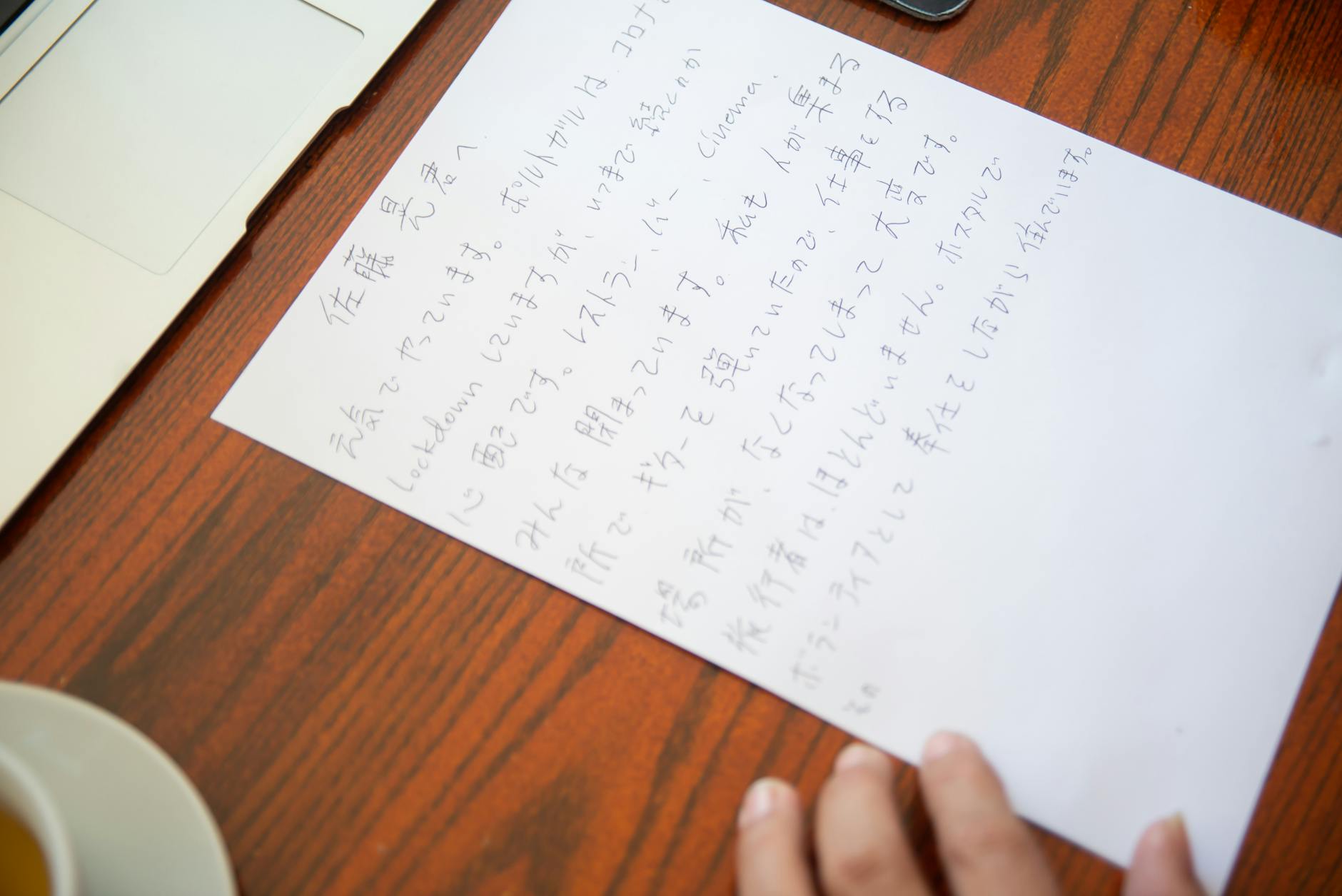 Close-up of a handwritten Japanese letter on a wooden desk with a laptop and tea cup.