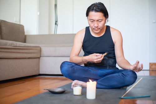 Free Asian man meditating using palo santo and candles indoors, embracing spirituality. Stock Photo