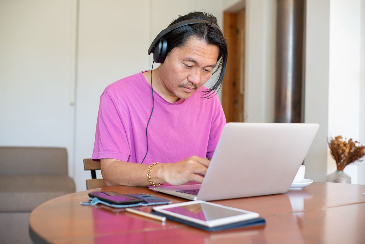 自宅でヘッドホンをつけてノートPCに向かい副業の作業をする男性