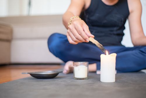 Free A man sits cross-legged indoors, lighting a candle for relaxation and meditation. Stock Photo