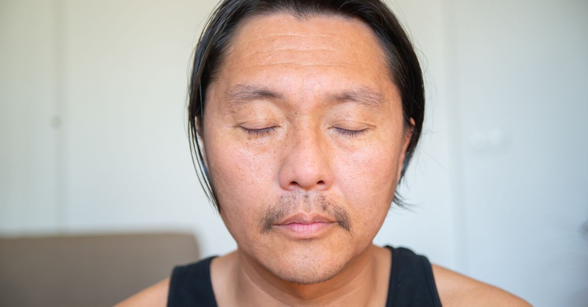 Close-up of an Asian man with closed eyes in a relaxed indoor setting, embracing peacefulness.