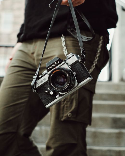 Close-up of a vintage camera being held by a person in casual attire, outdoors.