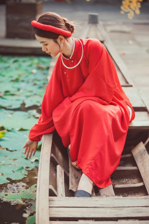 Free A Woman in Red Dress Sitting on a Wooden Boat Stock Photo
