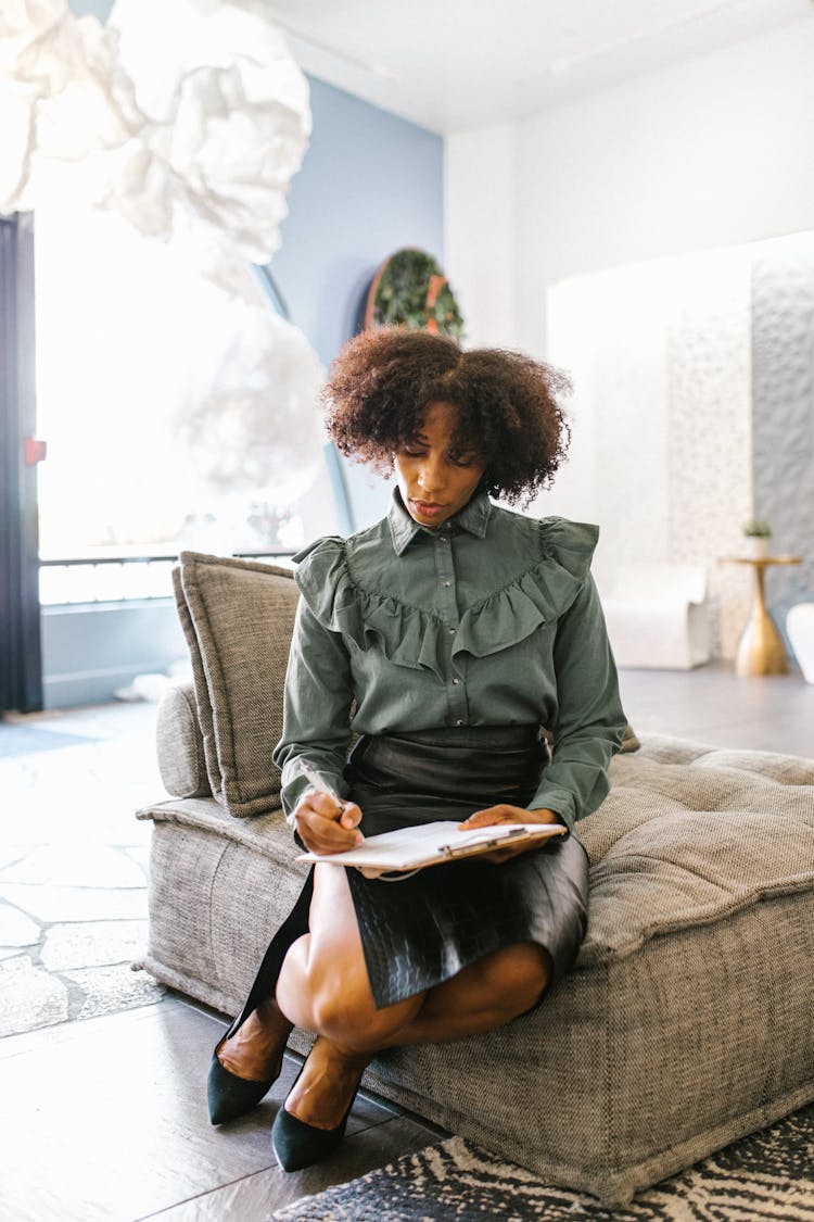 A Woman Sitting On A Gray Couch While Signing Contract