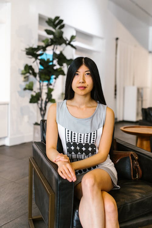 Woman in a Gray Sleeveless Dress Sitting on a Leather Chair