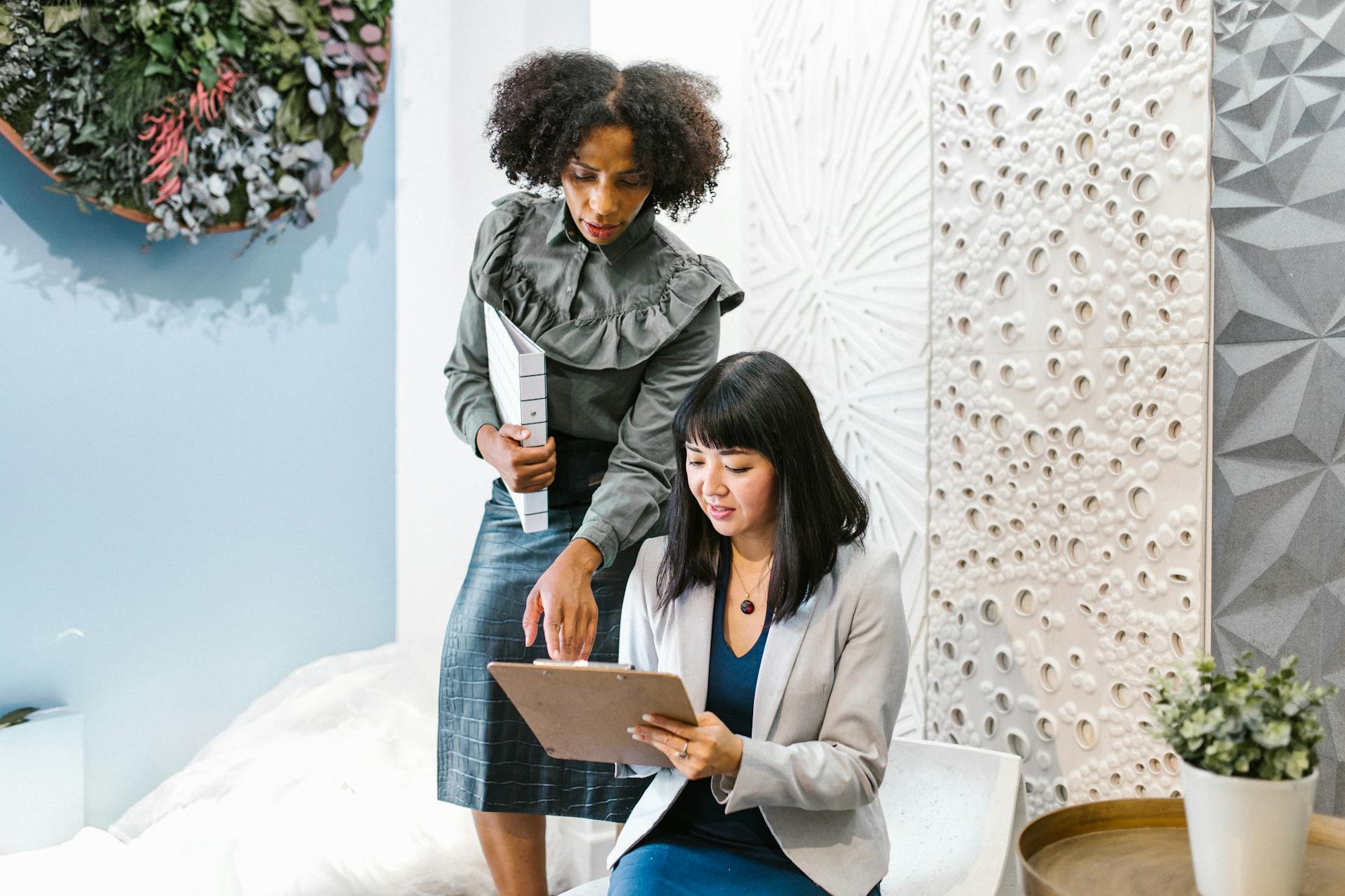 African American and Asian businesswomen discussing work in a stylish office setting.