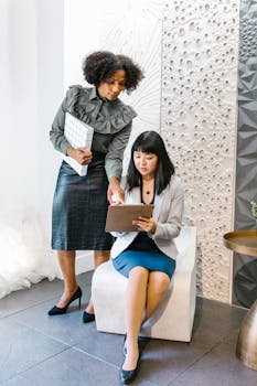 Two professional women discussing work in a stylish office setting, symbolizing women empowerment.