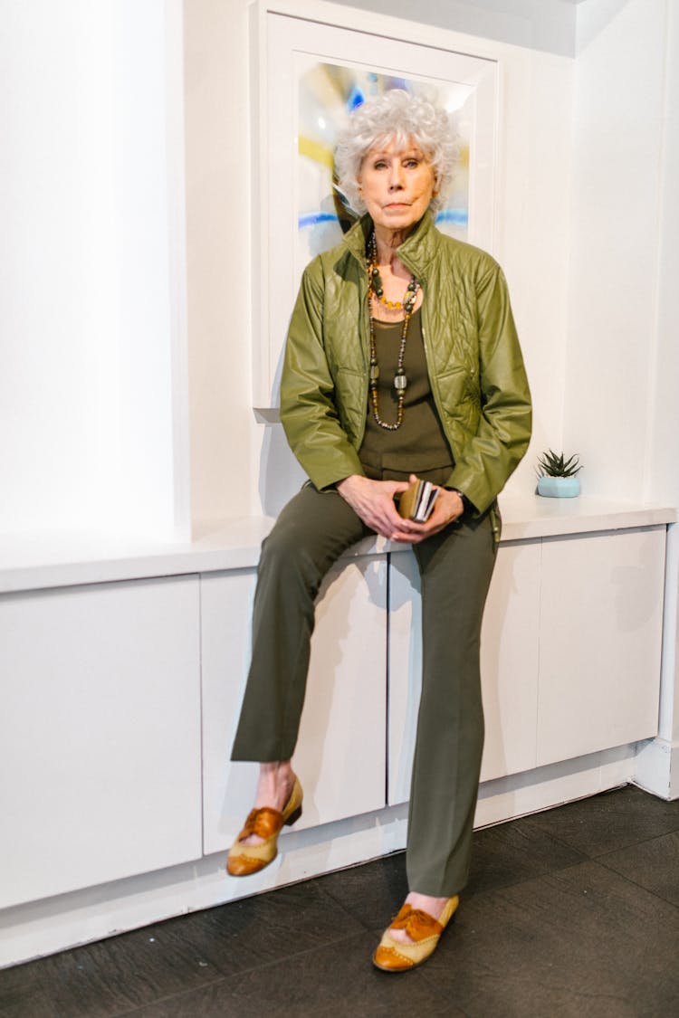 An Elderly Woman In A Green Outfit Sitting On A Cabinet