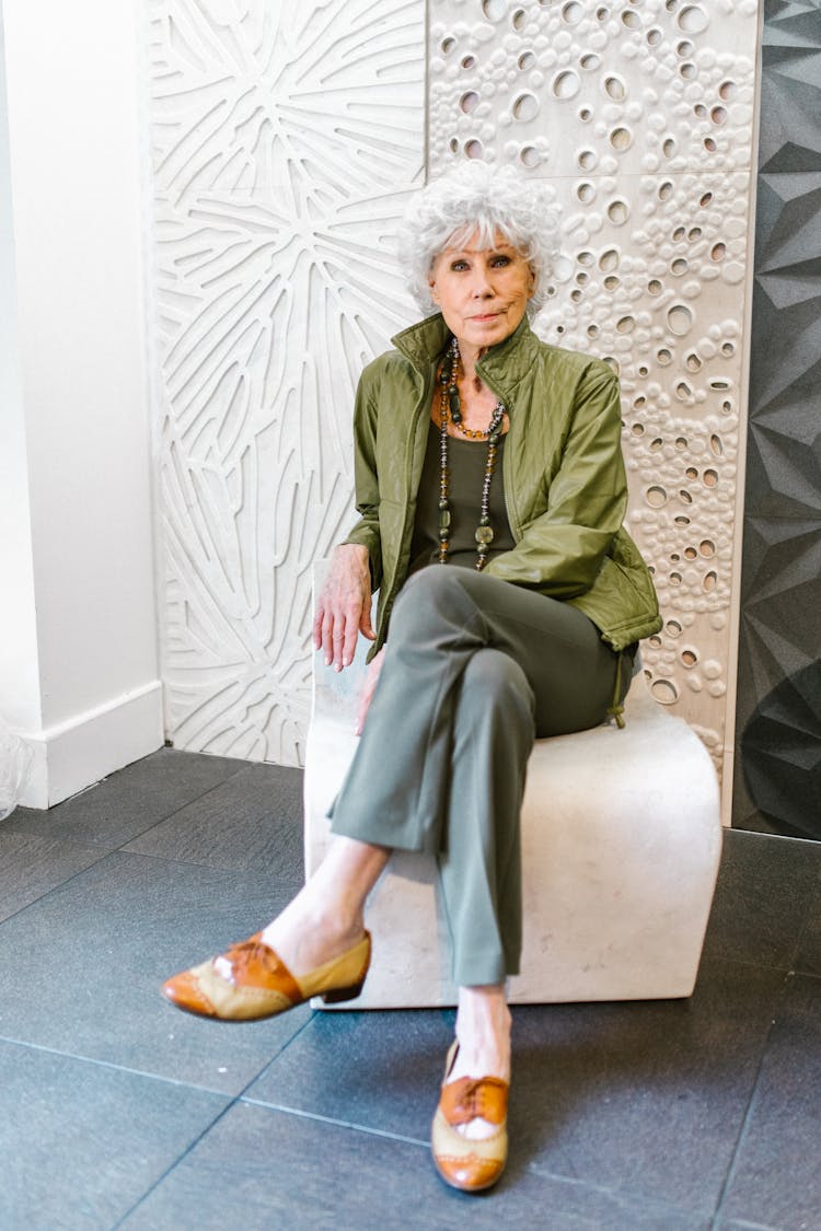 An Elderly Woman In A Green Outfit Sitting On A Chair