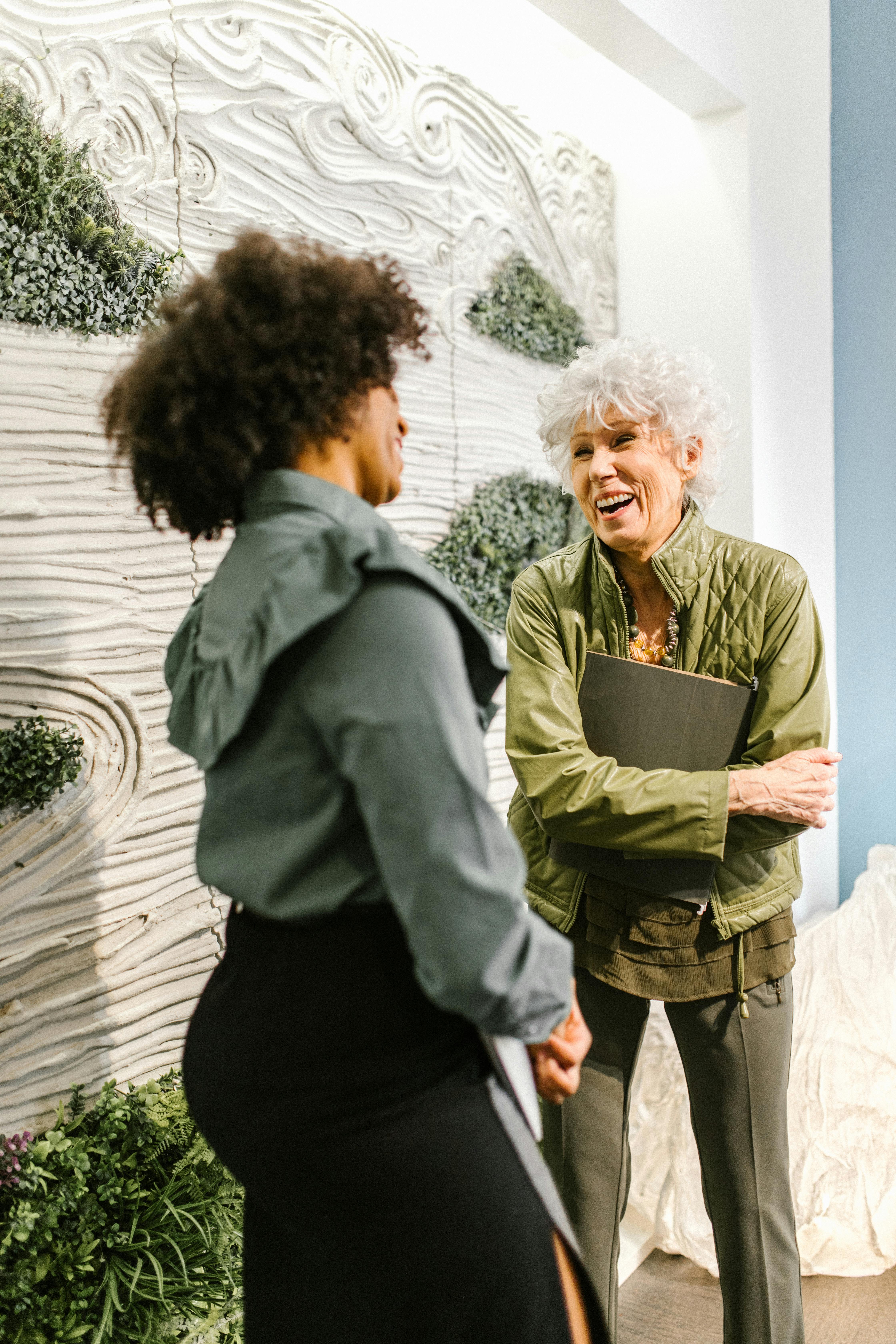 Two businesswomen, diverse in ethnicity, engaged in a lively conversation indoors, illustrating effective communication.