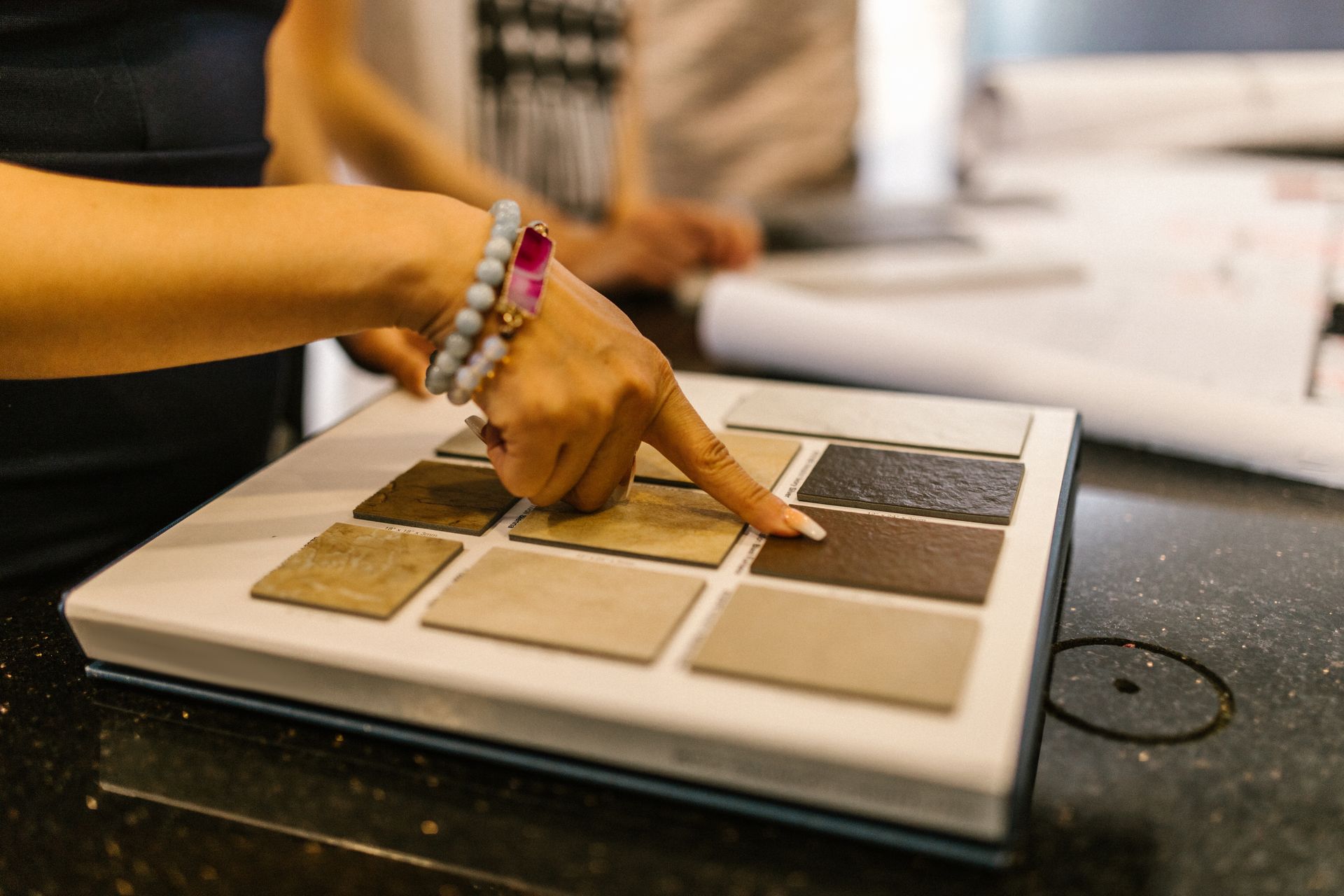 Close-up of a woman's hand selecting material samples in an office setting, showcasing design creativity.