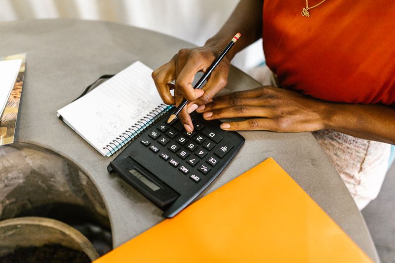 A Black woman’s hands working a calculator with a pencil, spiral notepad, and folder on the table. Working out what you can actually pay each month is the first step to finding therapy you can afford.