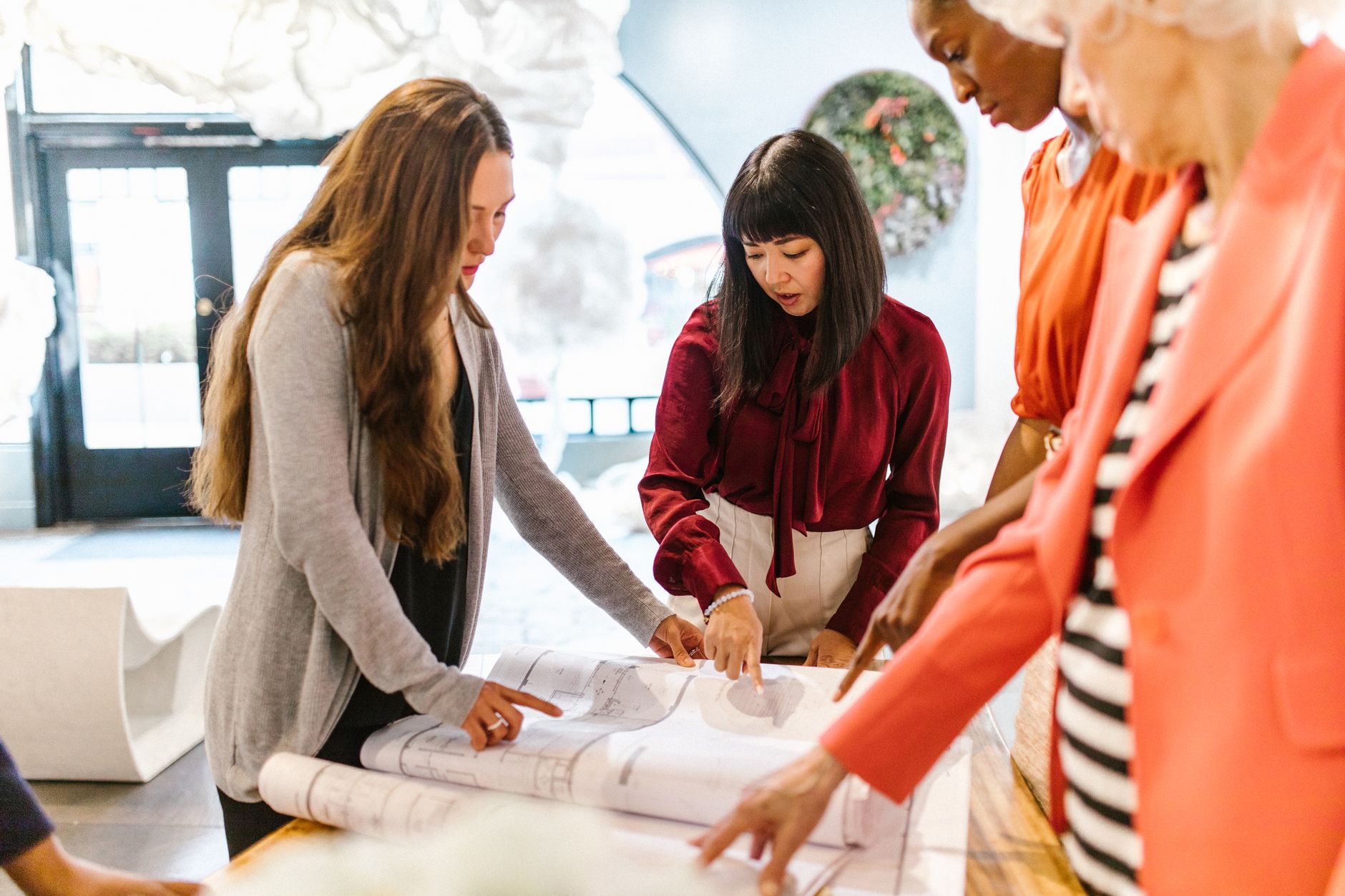 A diverse group of women in an office discussing plans and ideas around a table.