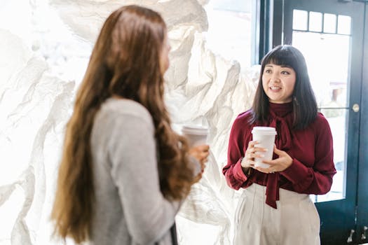 Two professional women having a conversation during a coffee break indoors.