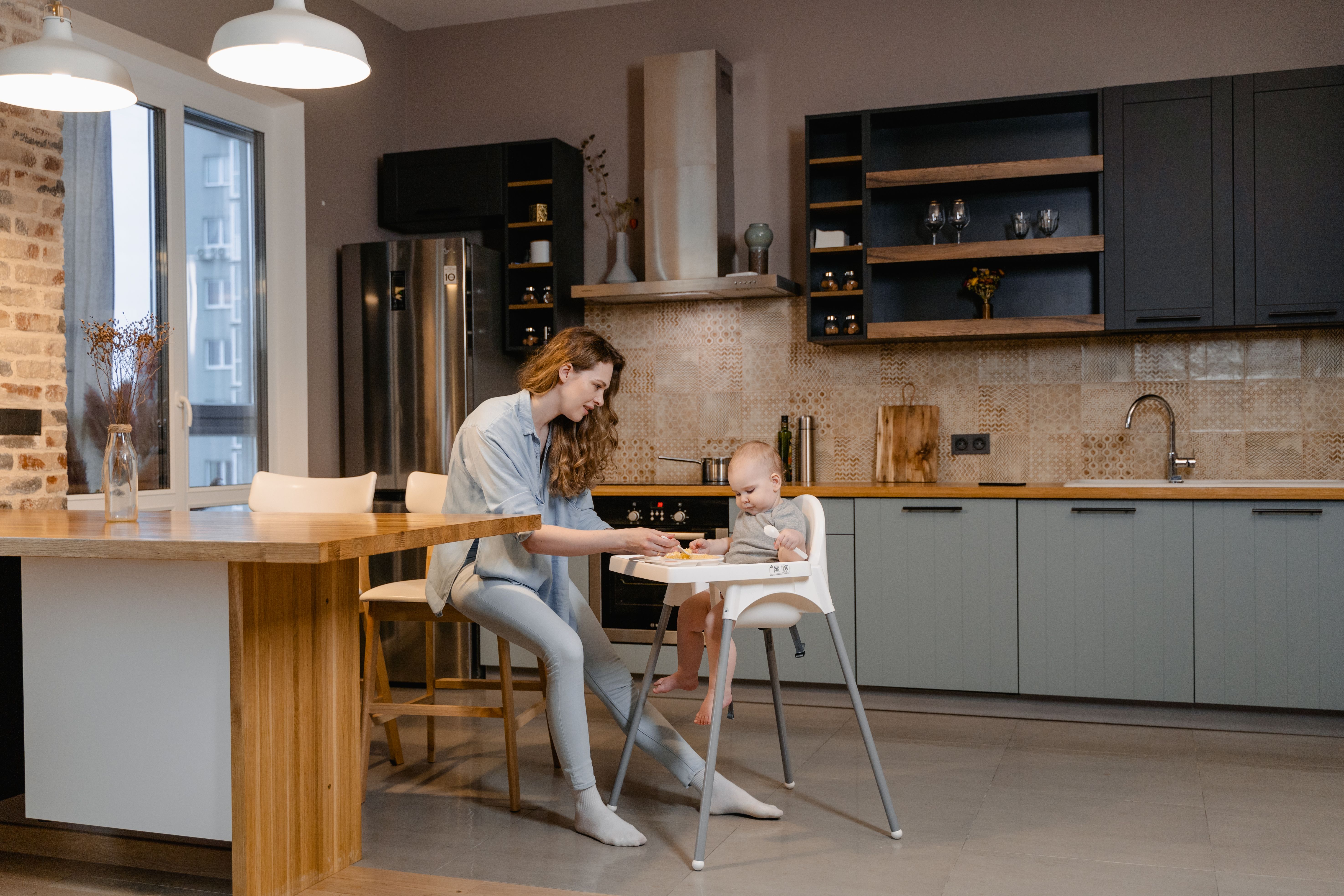 A mother feeds her toddler in a stylish, modern kitchen interior.