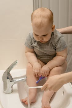 Cute baby sits in sink holding toothbrush, ready for toothbrushing. Captures a sweet daily routine moment.