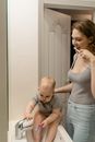 A Woman Brushing Her Teeth Together with Her Baby Sitting on the Sink