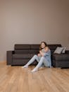 Woman in Blue Denim Jacket and White Pants Sitting on Brown Wooden Floor