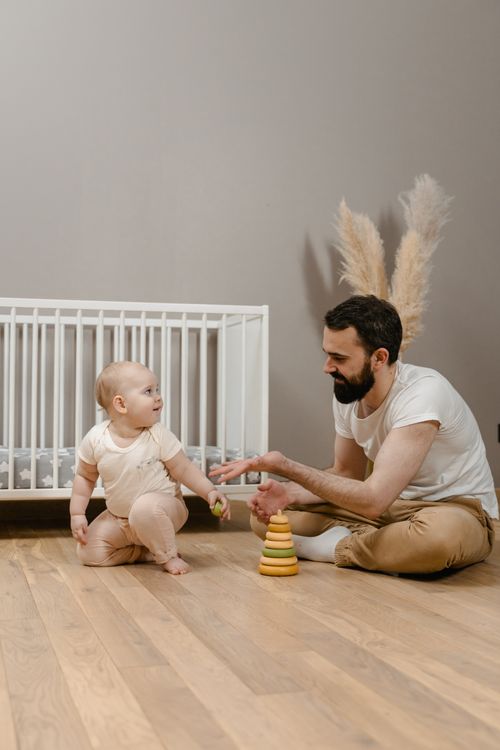 Free A father and baby enjoying playtime with toys on a wooden floor near a crib. Stock Photo