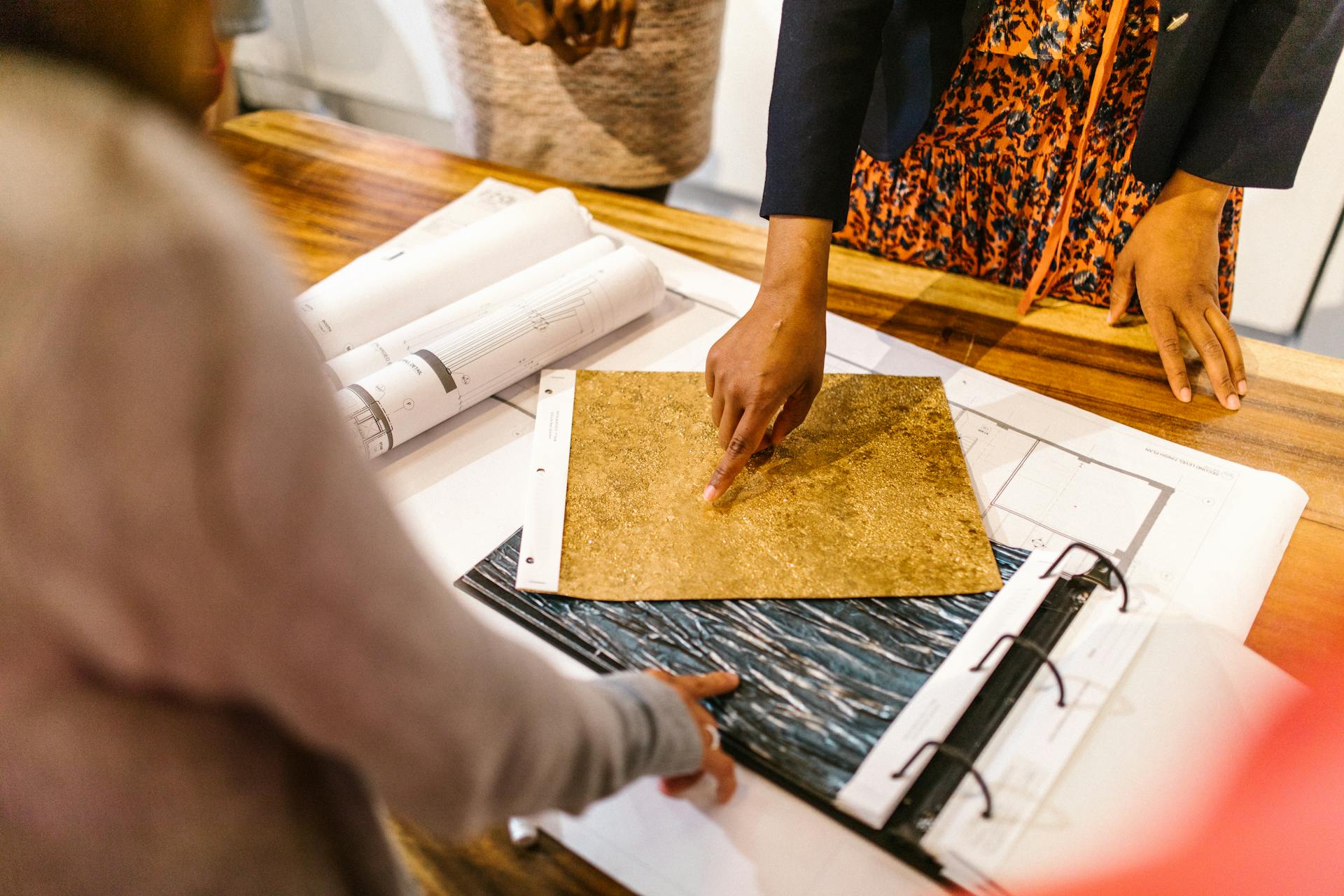 Group of designers evaluating fabric and material samples on a wooden table in an office setting.