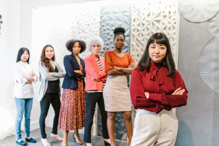 A Woman In Red Long Sleeves Standing With Her Arms Crossed With People Standing Behind Her