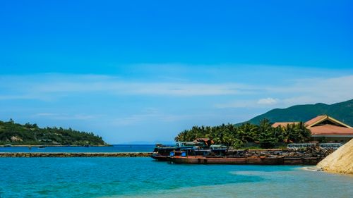 Free A vibrant coastal scene with boats docked, lush greenery, and mountains under a clear blue sky. Stock Photo