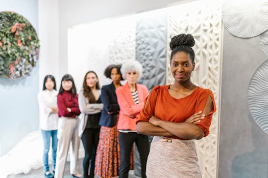 A confident female leader stands with diverse female colleagues in a modern office setting.