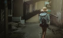 白天，一位背着背包的年轻女子漫步在一条安静的城市小巷里